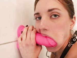 Teenage slut is blowing a yam-sized pinkish lovemaking toy that's stuck to a wall